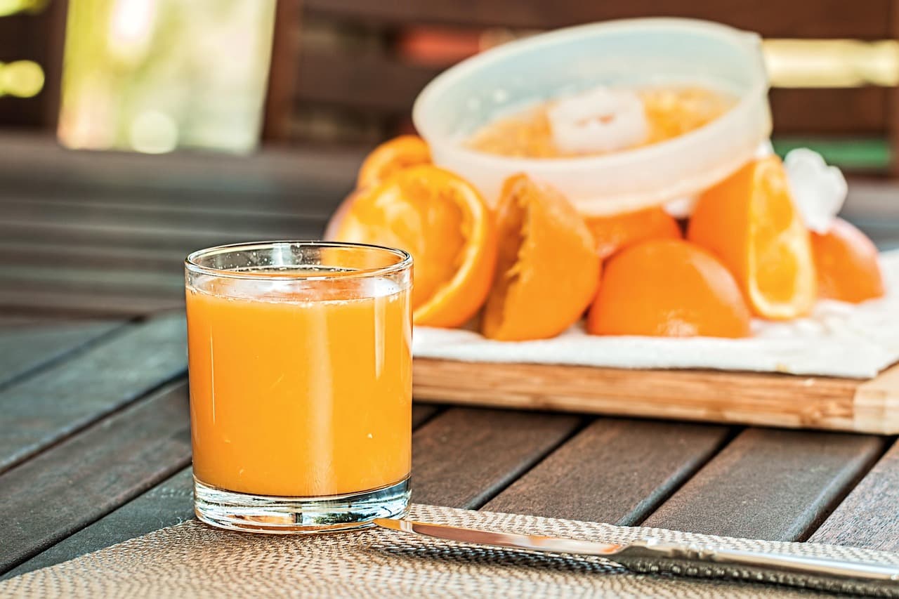 A glass of fresh orange juice beside halved oranges on an outdoor table